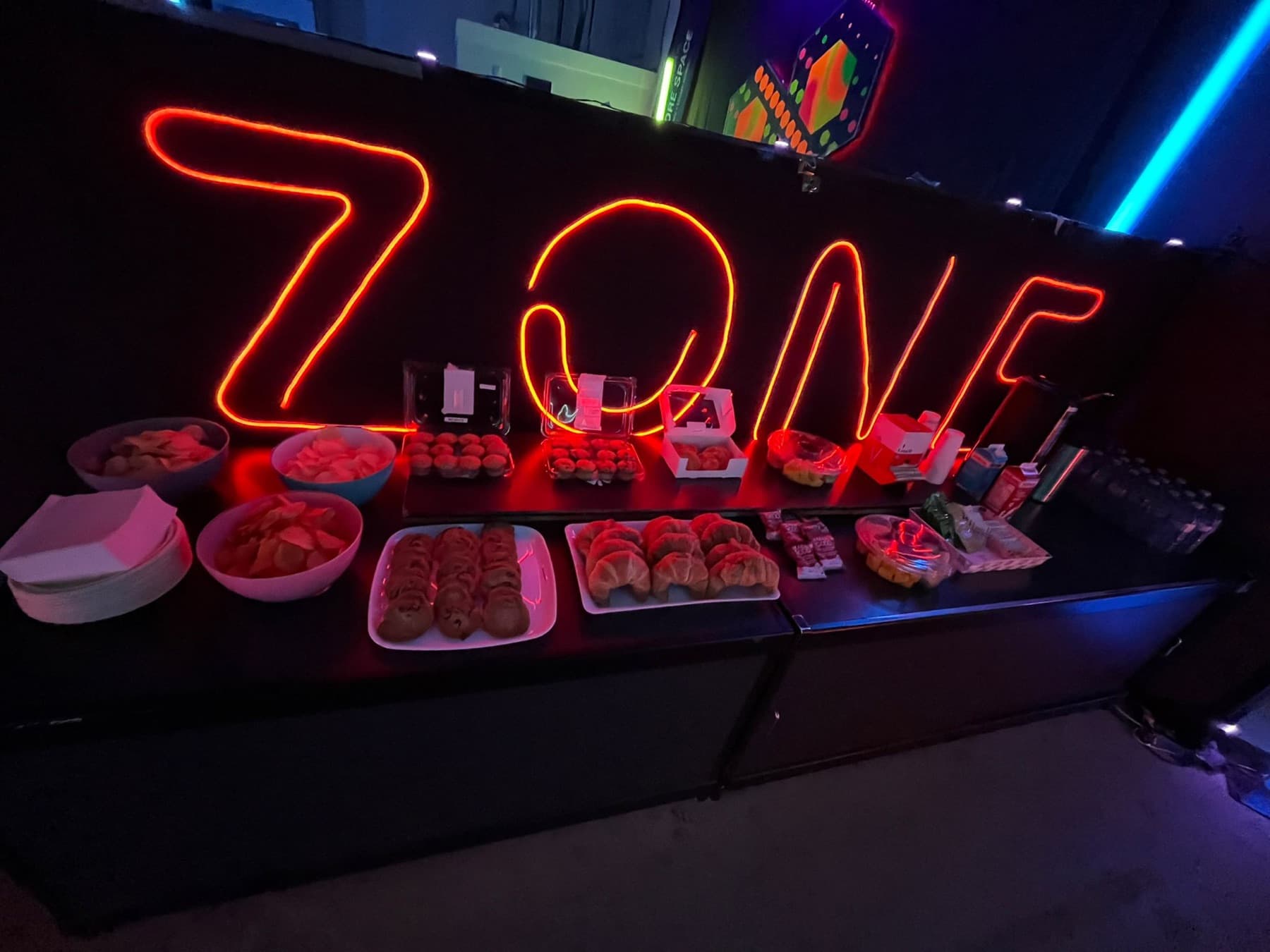 A catering spread of snacks and drinks under a neon sign