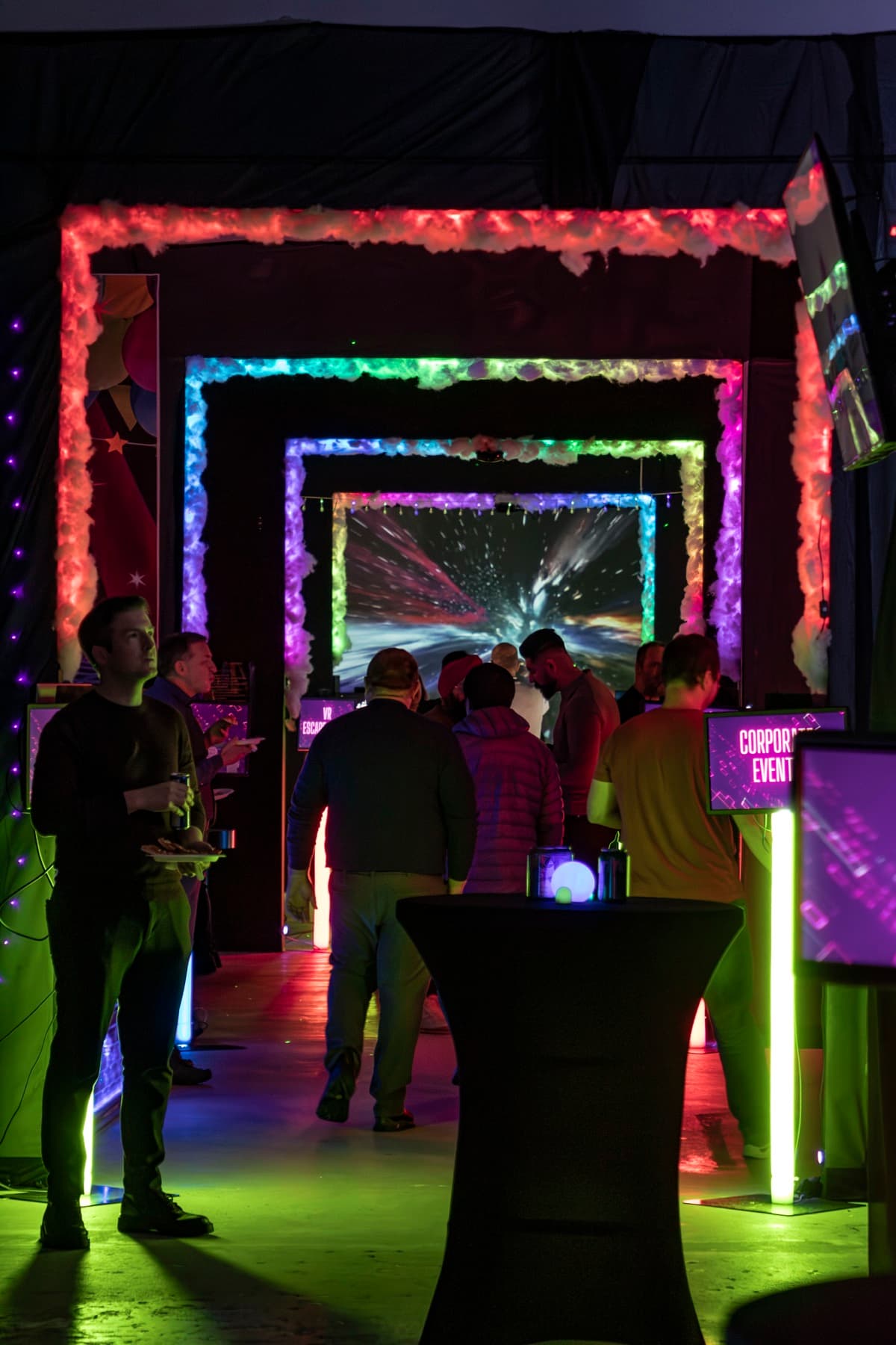 A crowd of guests mingling with drinks under lit arches at a large company party